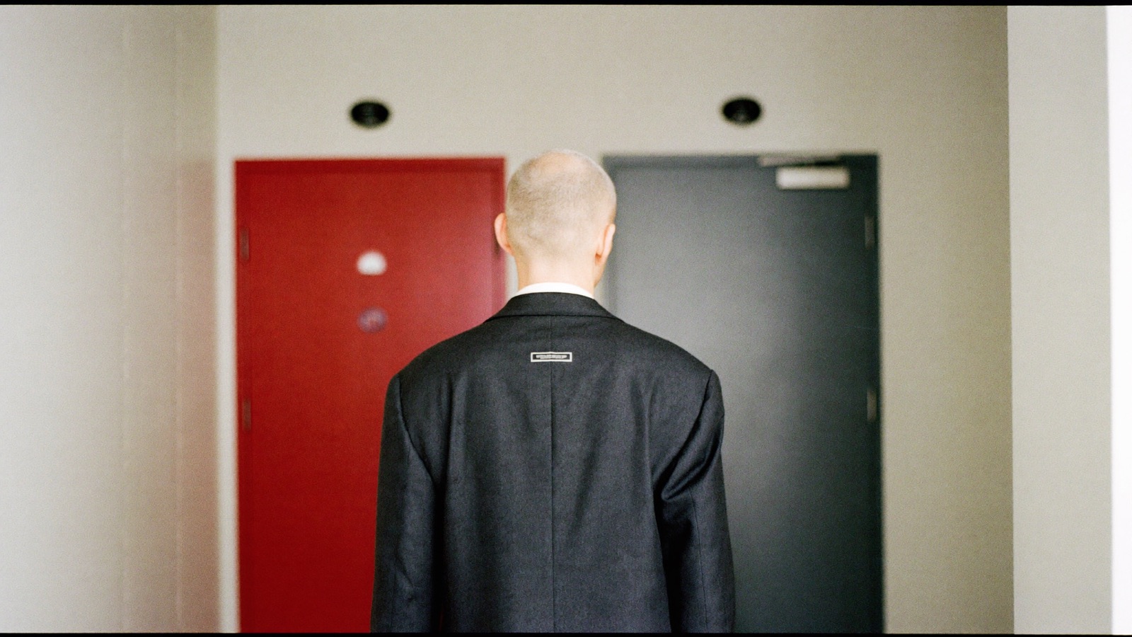 A business owner in a quiet corridor facing two closed doors, one red and one grey.
